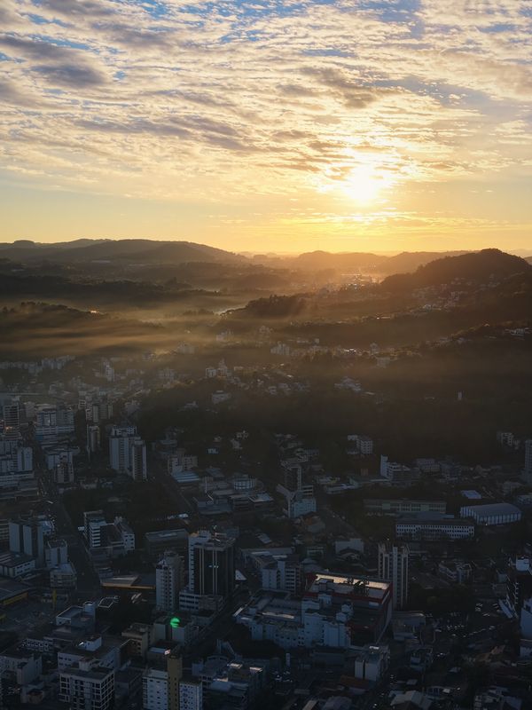 O sol nascendo atrás dos morros com névoa sobre a cidade de Concórdia