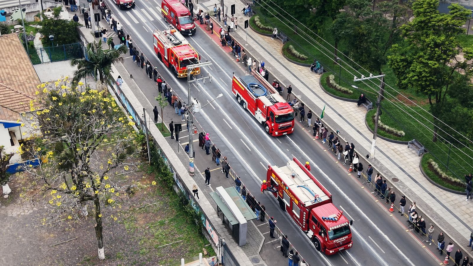 Caminhões dos bombeiros no desfile de 7 de Setembro em Concórdia, com o público na calçada, vistos do alto